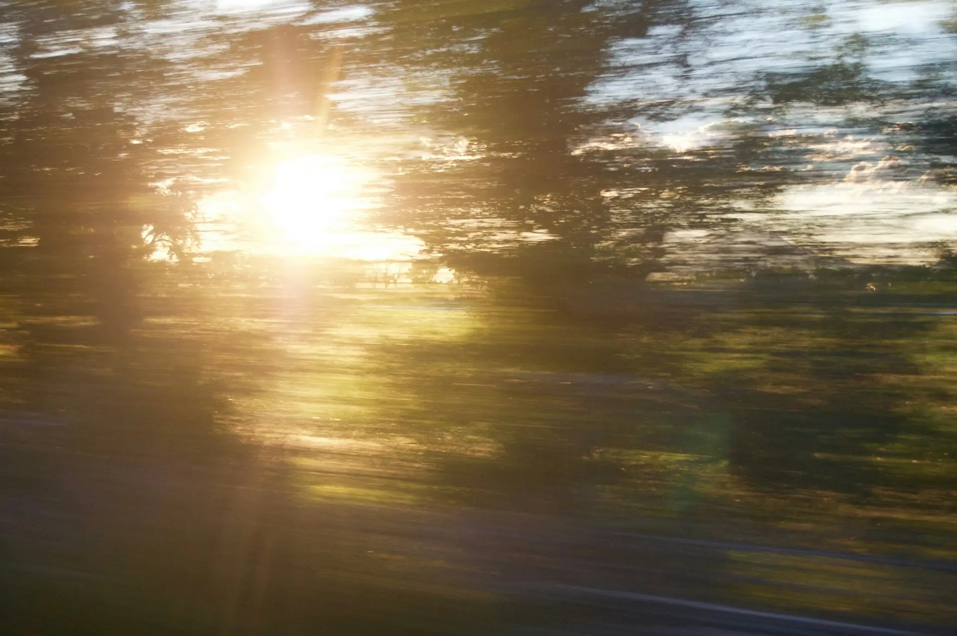 Sunlight breaking through trees with a warm, blurred motion effect across a landscape scene.