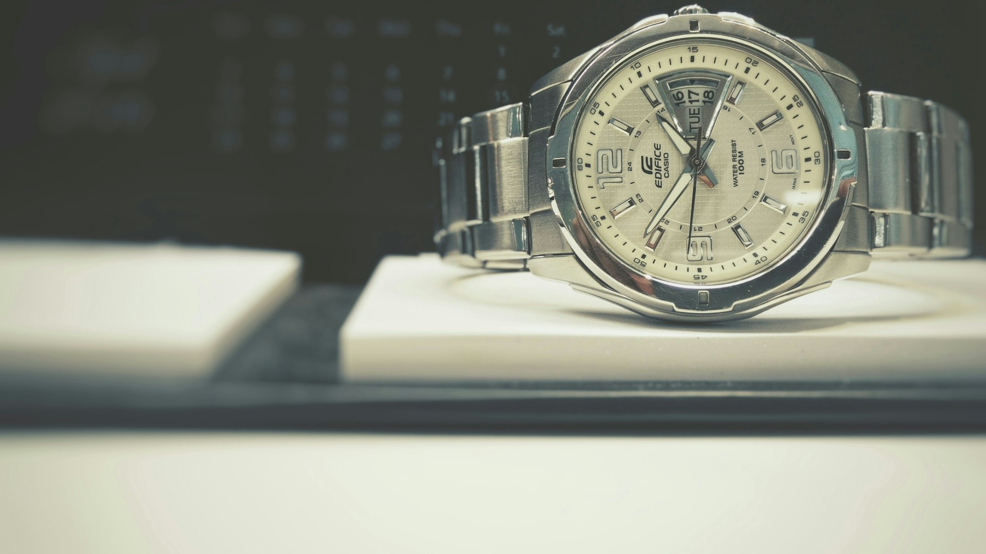 Stainless steel automatic wristwatch with a white dial, silver hour markers, and a metal bracelet resting on a white surface.