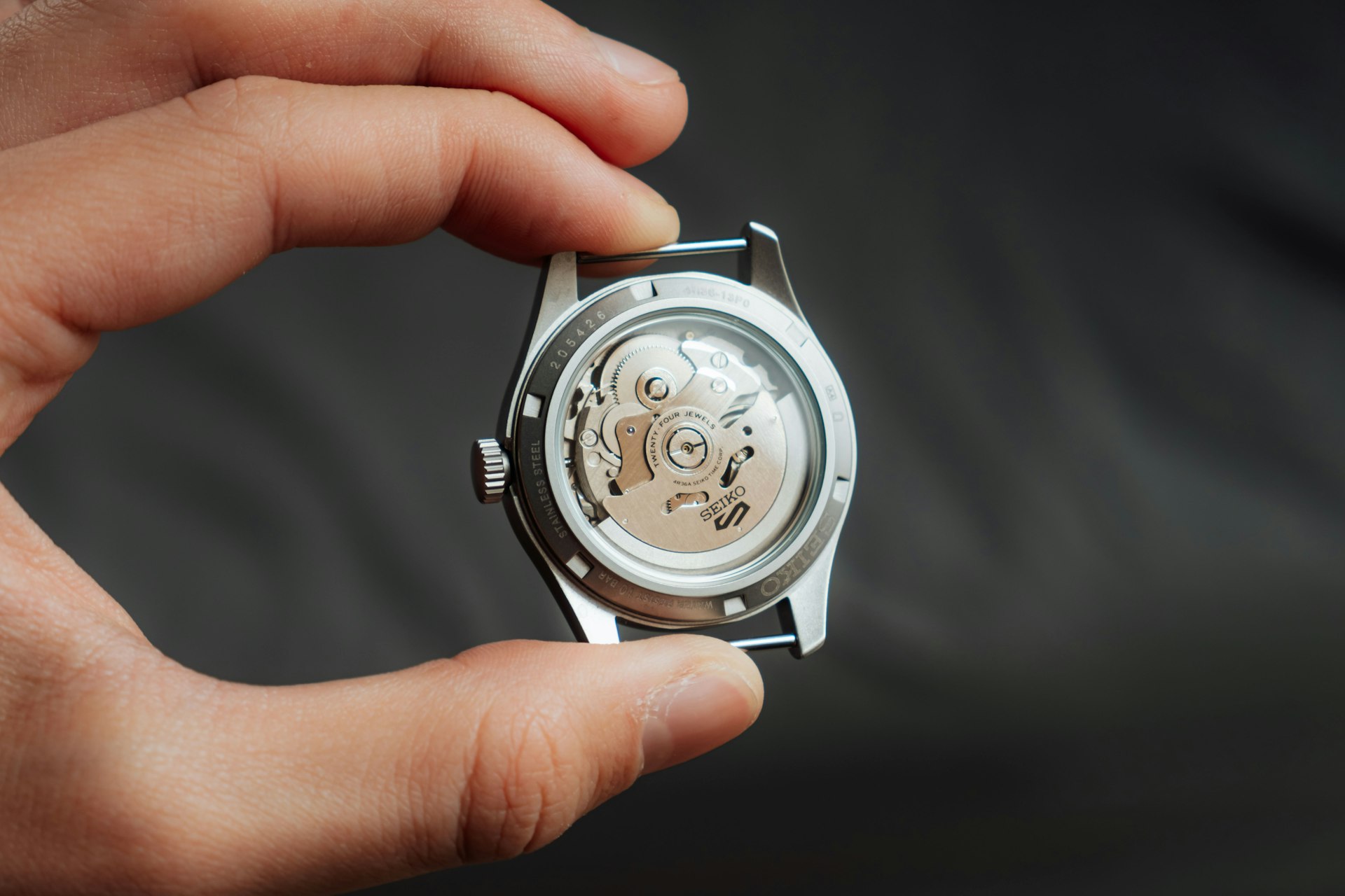 Close-up of a transparent caseback automatic watch held between fingers, revealing the intricate mechanical movement.