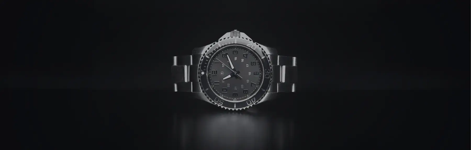 Close-up of a stainless steel automatic wristwatch with a dark dial, rotating bezel, and metal bracelet displayed against a dark background.