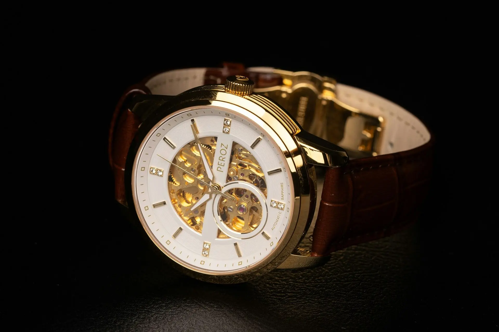 Gold wristwatch with a brown leather strap, white face, and visible internal gears, displayed on a black background.