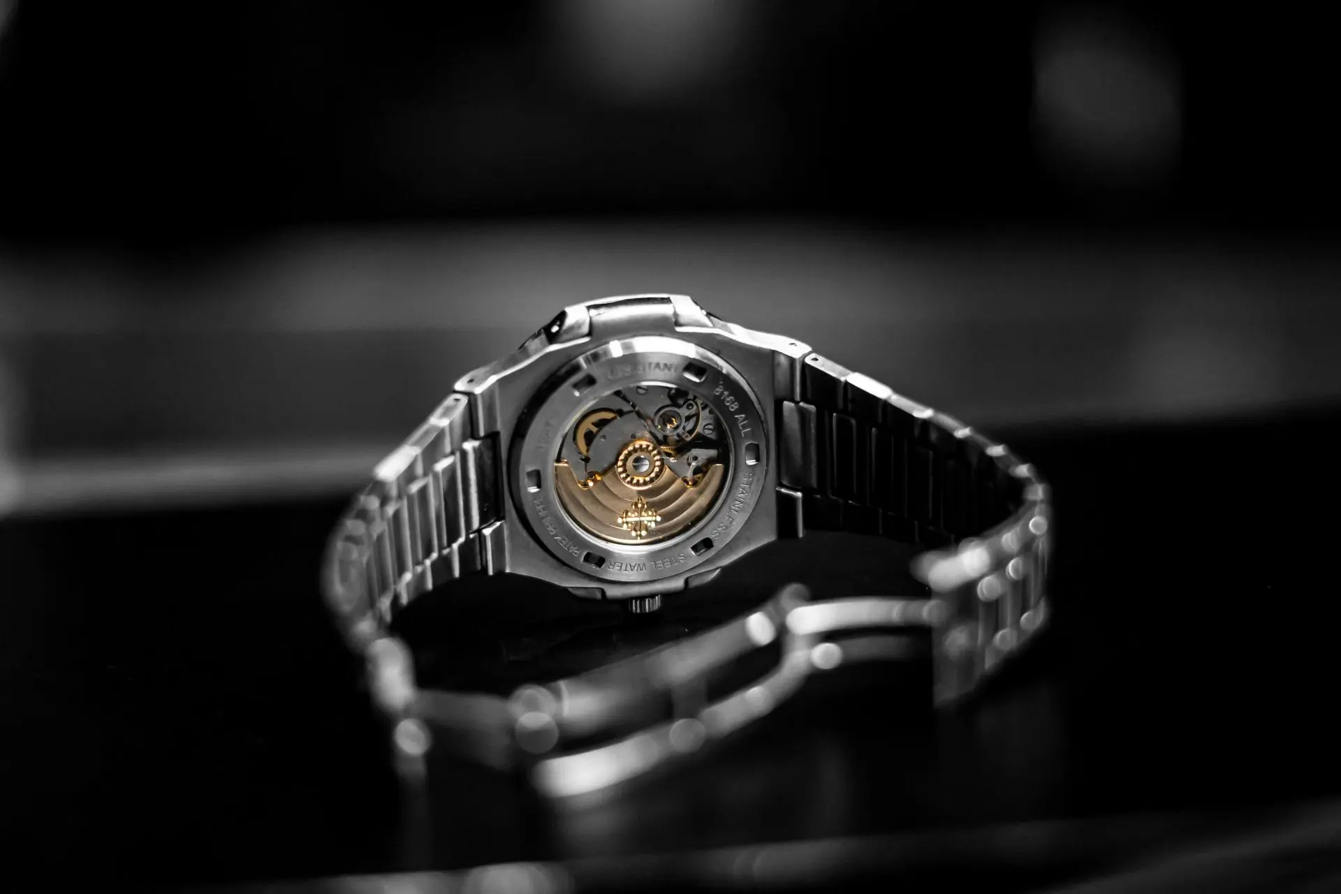 A close-up view of a silver wristwatch with an exposed mechanical movement, showcasing gears and components, placed on a dark surface.