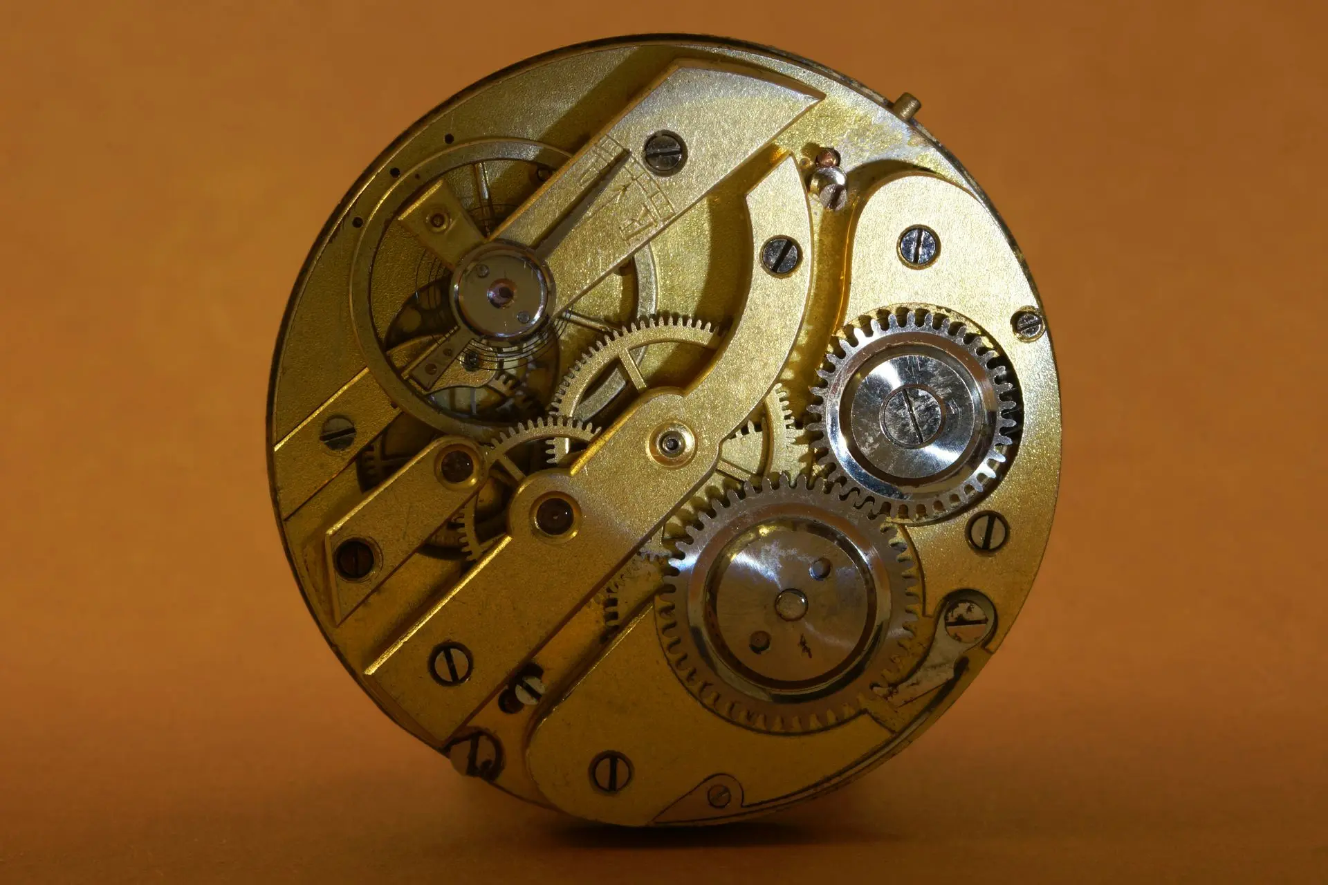 Vintage mechanical watch movement Close-up of a gold-colored mechanical watch movement showing gears, springs, and intricate components against a brown background.