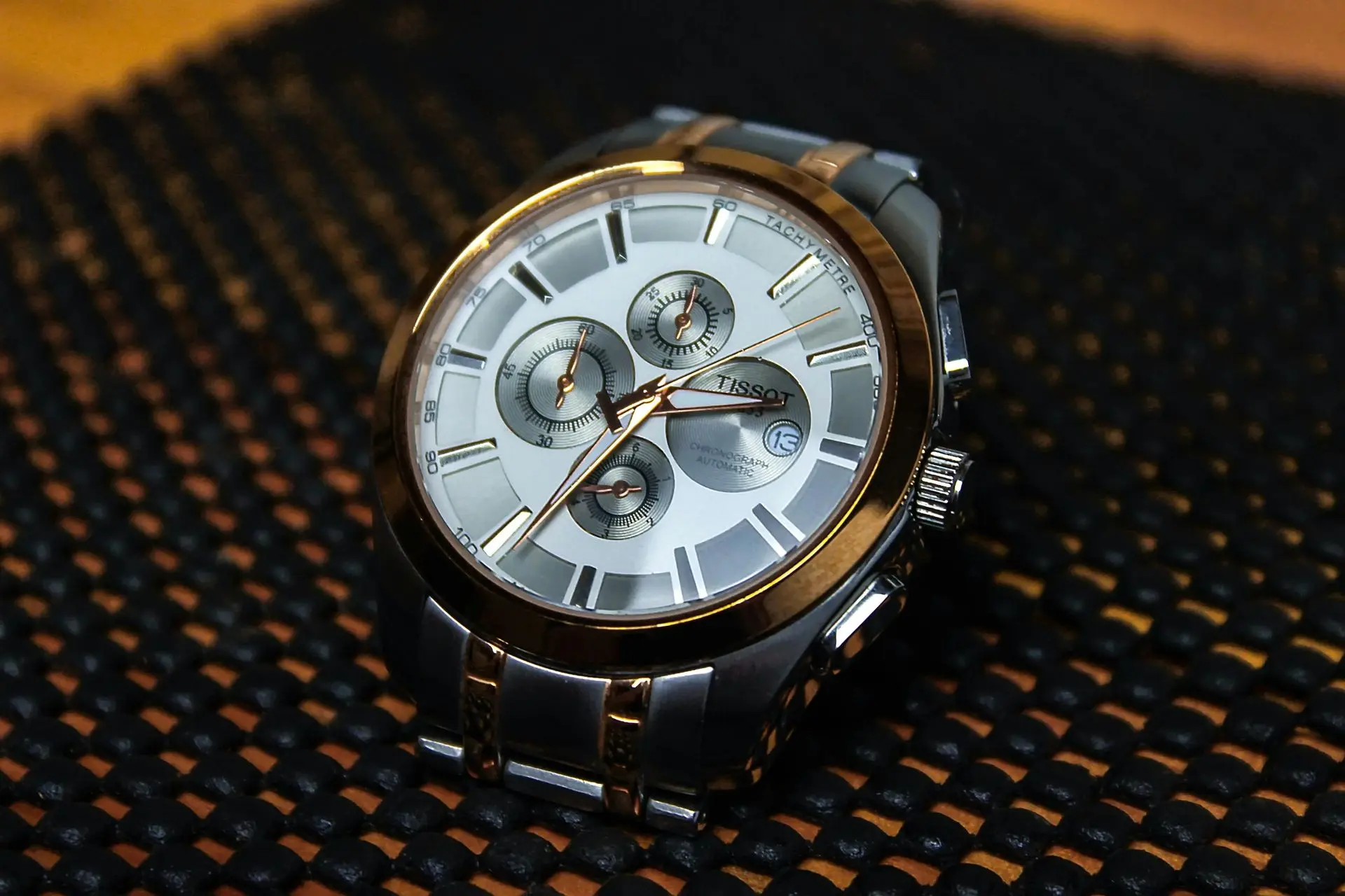 Tissot chronograph wristwatch with gold bezel and silver dial A silver and gold Tissot wristwatch with a white dial, three subdials, and a date display, placed on a textured black surface.