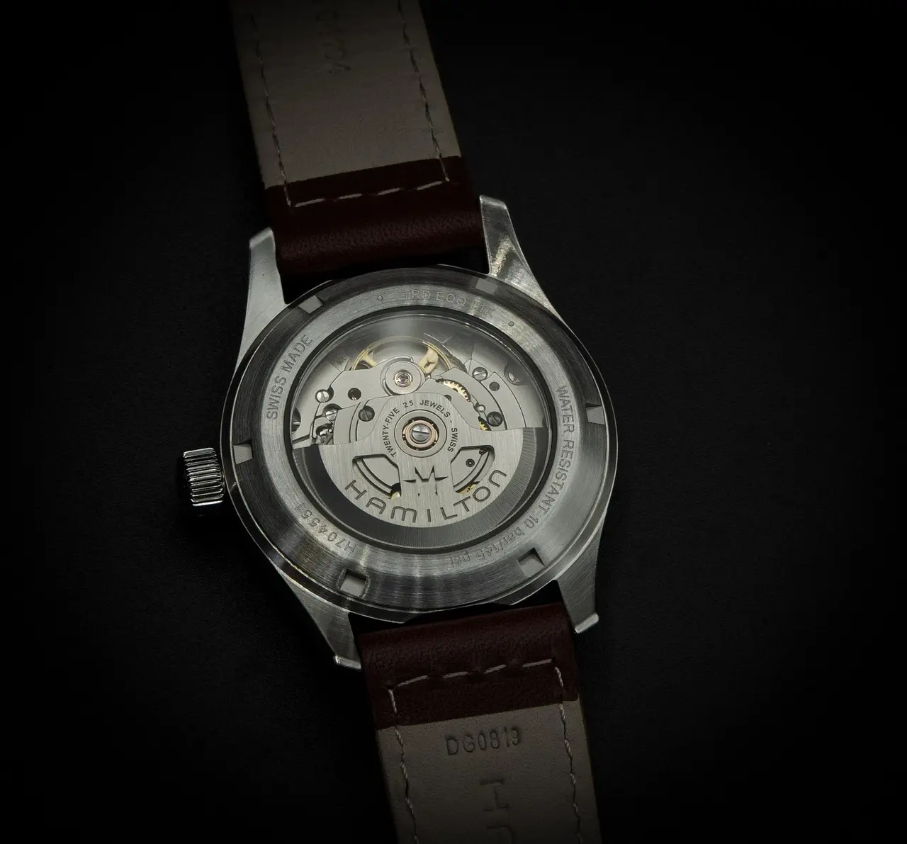 Close-up view of an ETA 2824-2 automatic movement inside a stainless steel watch case, with visible gears and rotor, seen through a transparent case back and brown leather strap