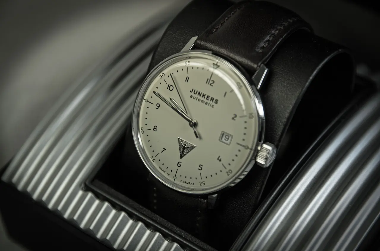 A Junkers automatic wristwatch with a white dial, black numerals, date window, and black leather strap displayed on a black cushioned stand.