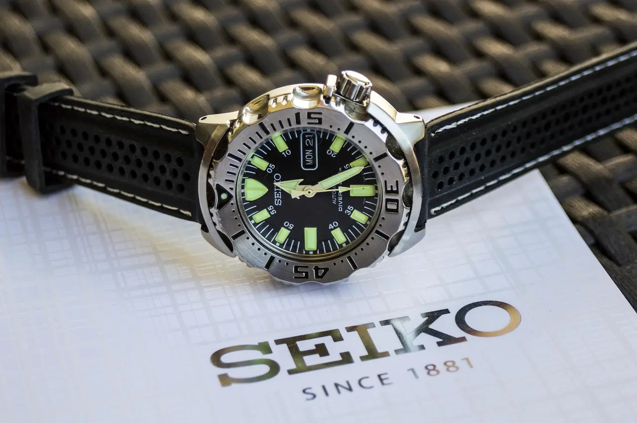 Close-up of a Seiko automatic wristwatch with a black dial, luminous markers, and a perforated black strap resting on a Seiko card.