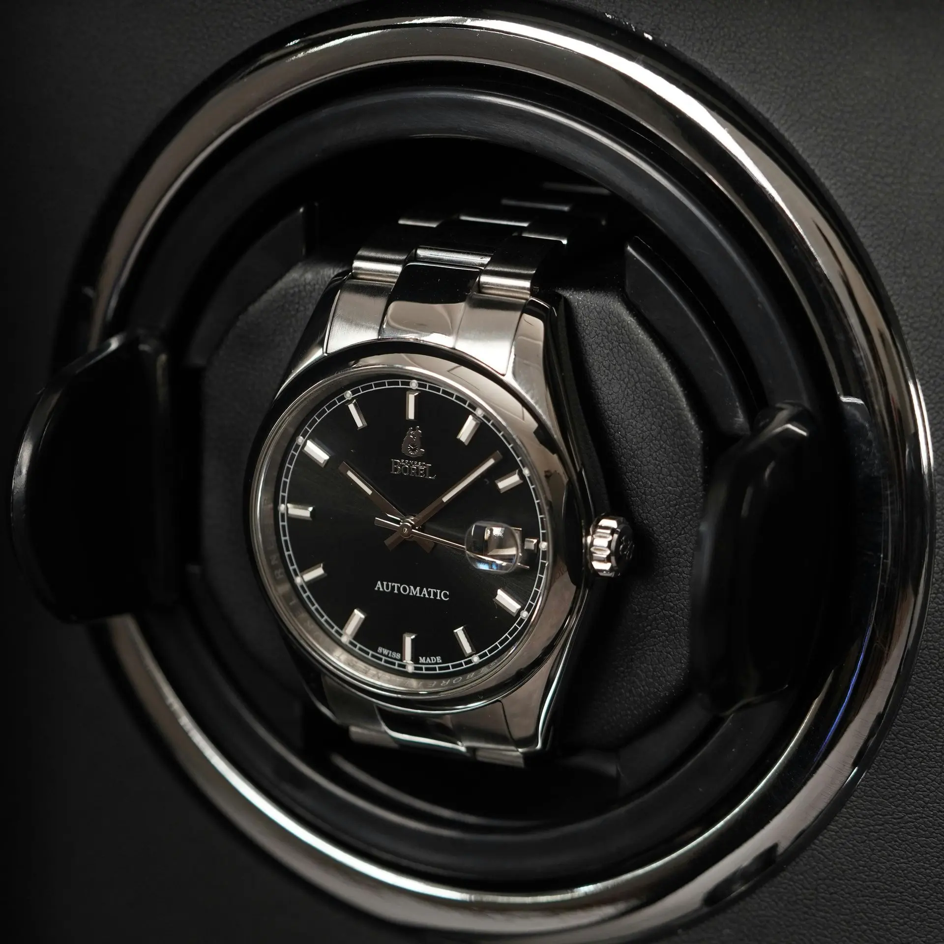A silver and black automatic wristwatch is secured in a black circular watch winder.