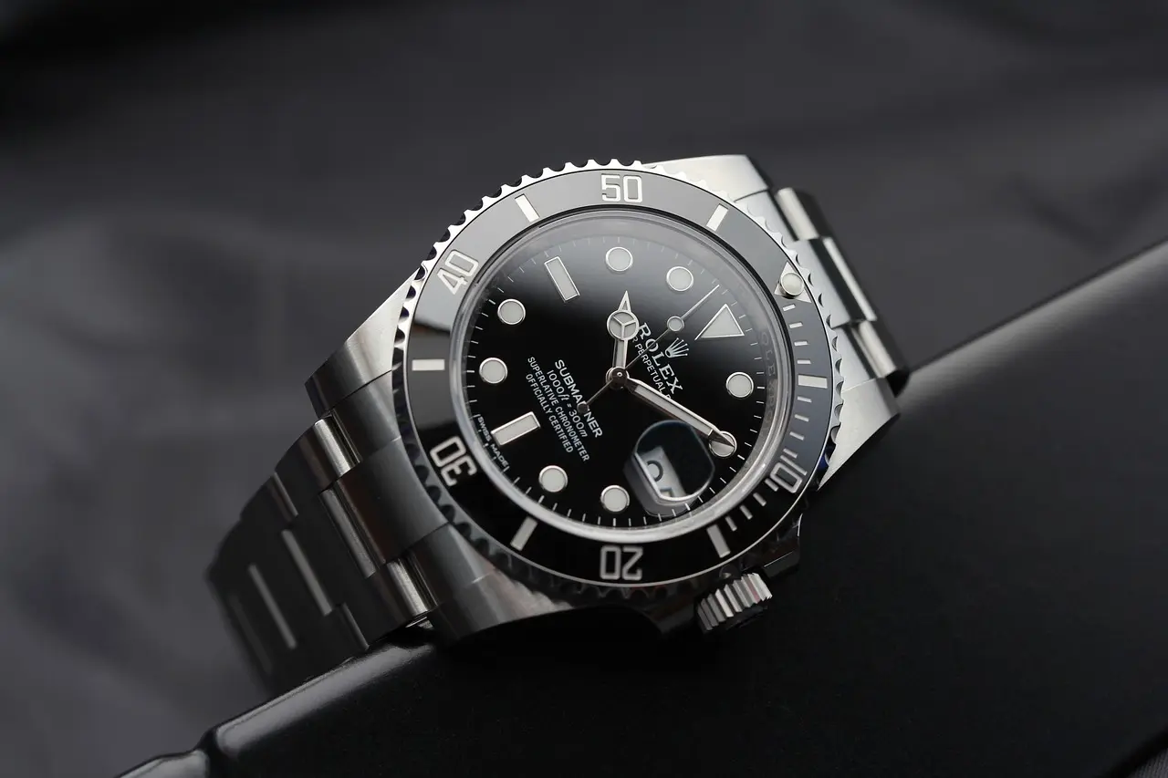 A close-up of a stainless steel Rolex Submariner watch with a black dial and bezel, featuring luminous markers and a date window, resting on a dark surface.
