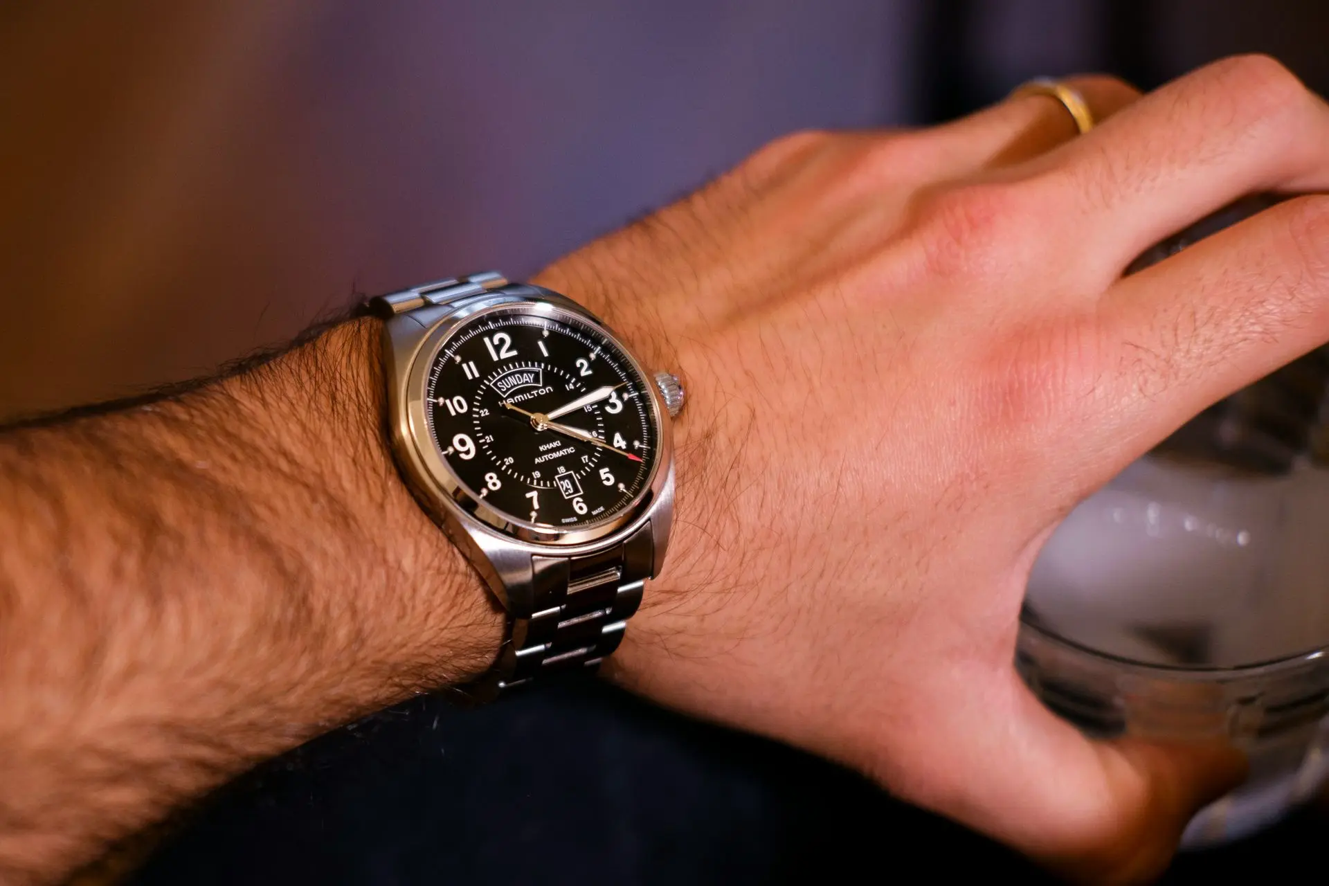 A close-up image of a Hamilton Khaki Field Mechanical watch with a black dial and stainless steel bracelet, worn on a person's wrist.