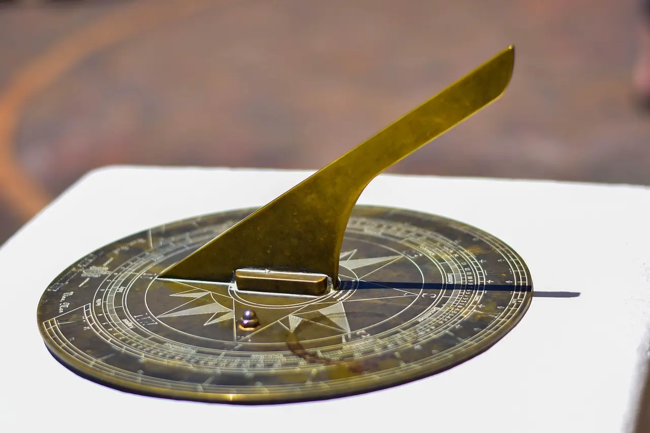 A brass sundial sits on a white surface outdoors, casting a shadow to indicate the time.