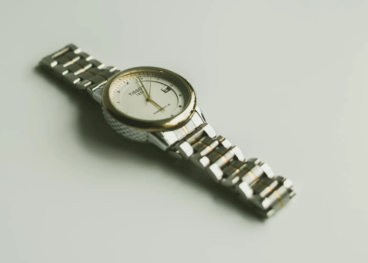 Tissot Two-Tone Gold and Steel Classic Watch Tissot two-tone dress watch with polished gold bezel, white/silver dial, gold baton markers, and date window on a steel and gold bracelet.