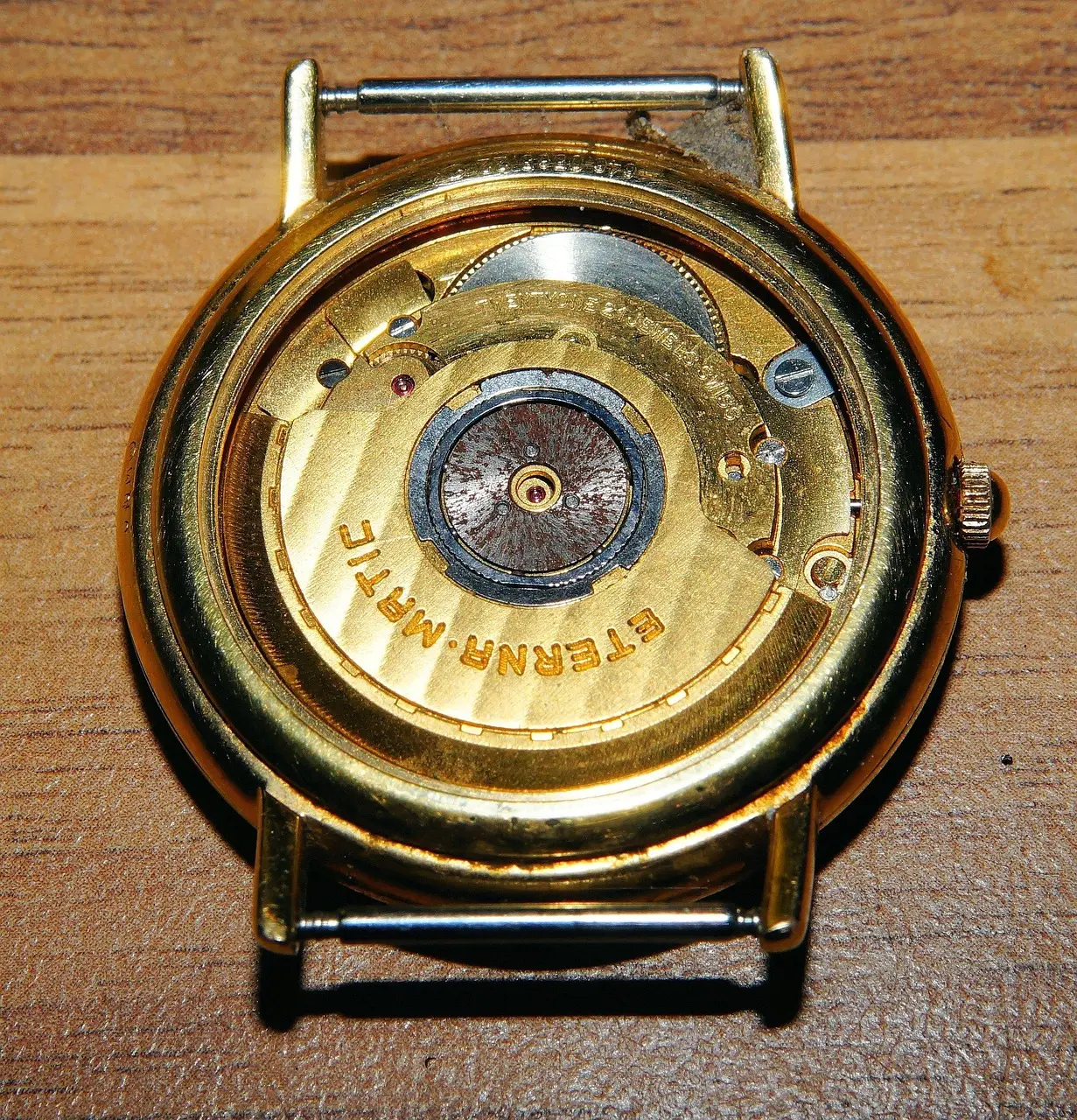 Back view of a gold-toned automatic watch movement, featuring the central oscillating rotor and "Swiss Made" engraving.