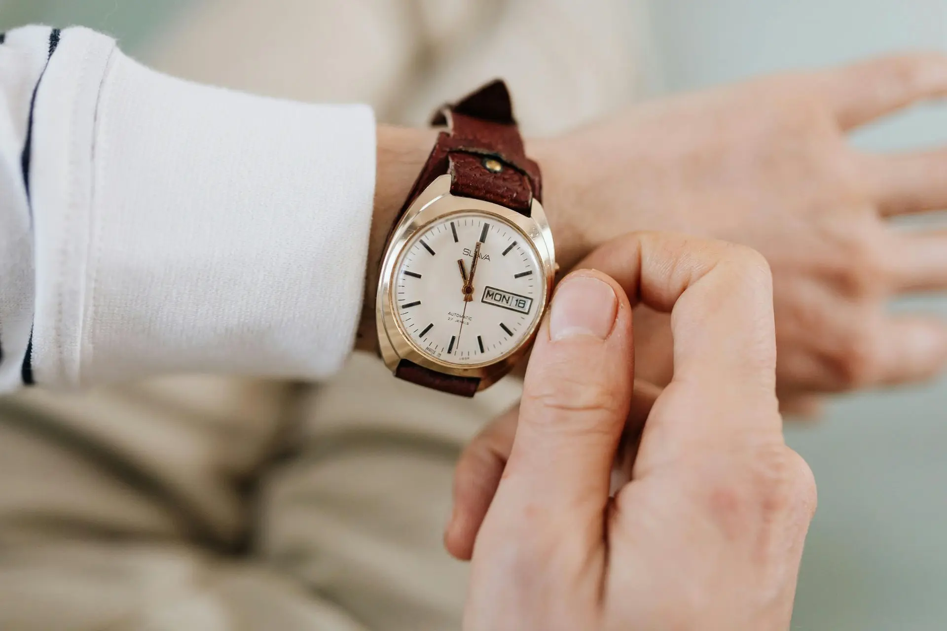 Close-up of a person's wrist wearing a vintage gold-tone automatic watch with a brown leather strap, while checking the time.