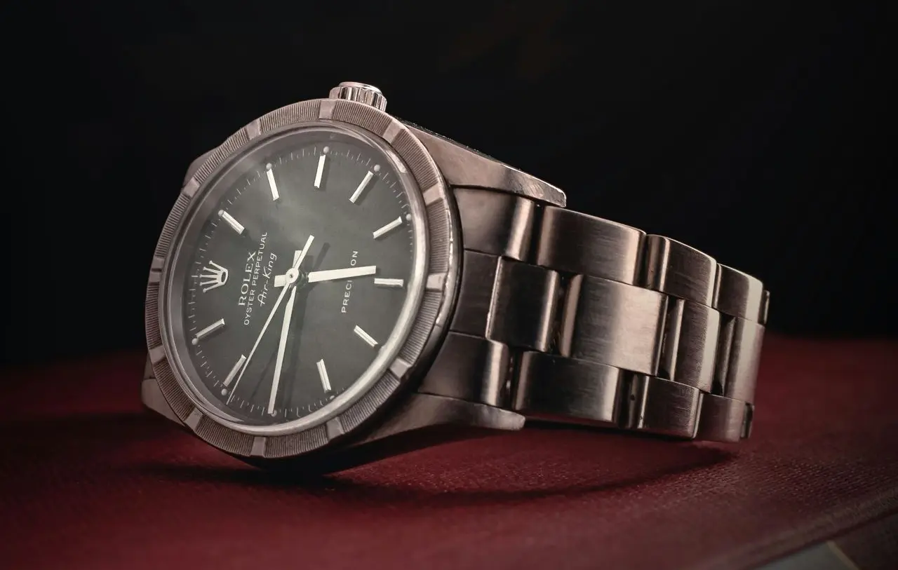 Vintage wristwatch with a distressed metal band and dark dial, resting on a red surface against a black background