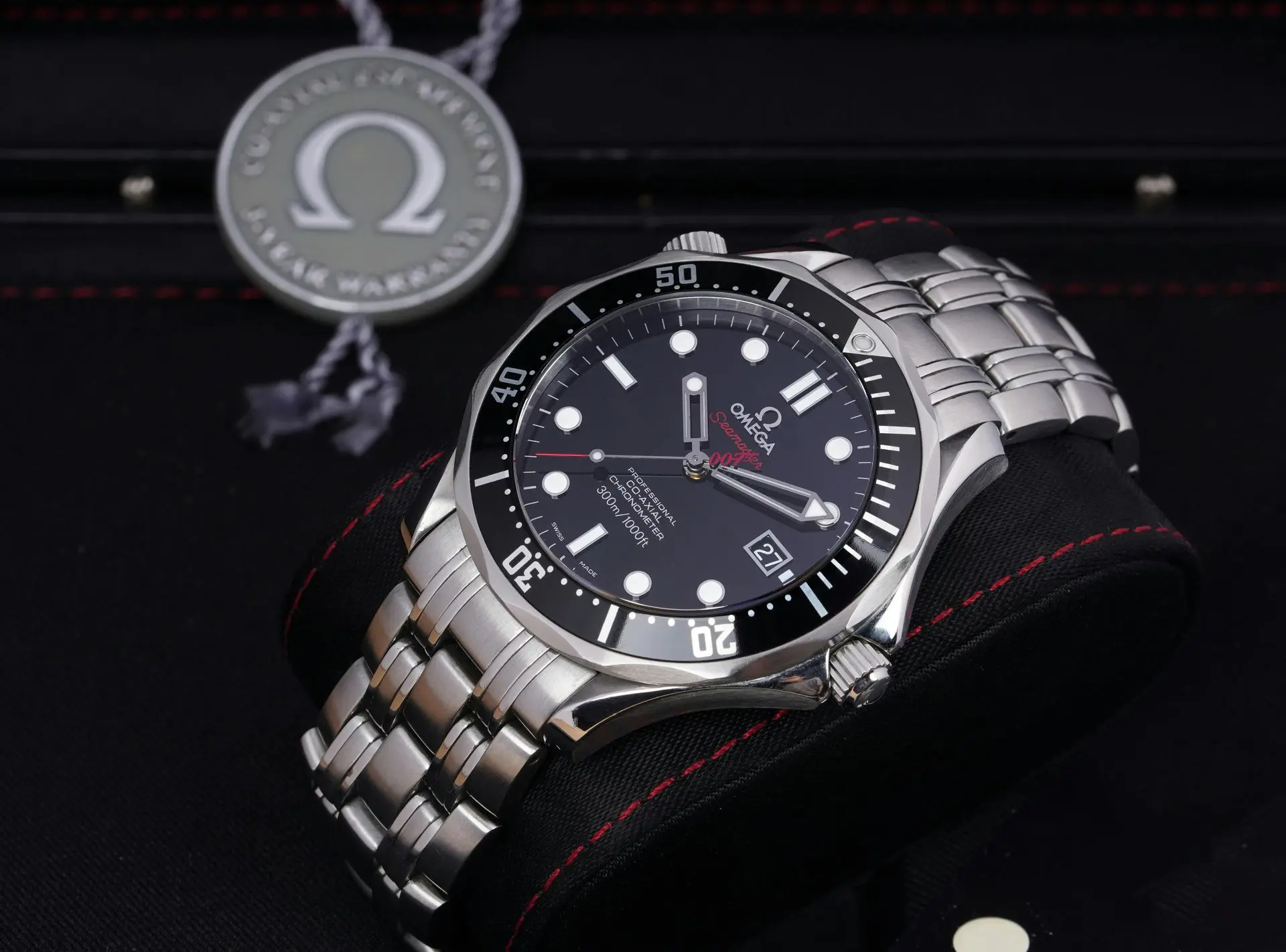 Omega Seamaster-style stainless steel dive watch with black bezel and metal bracelet, resting on a cushion.