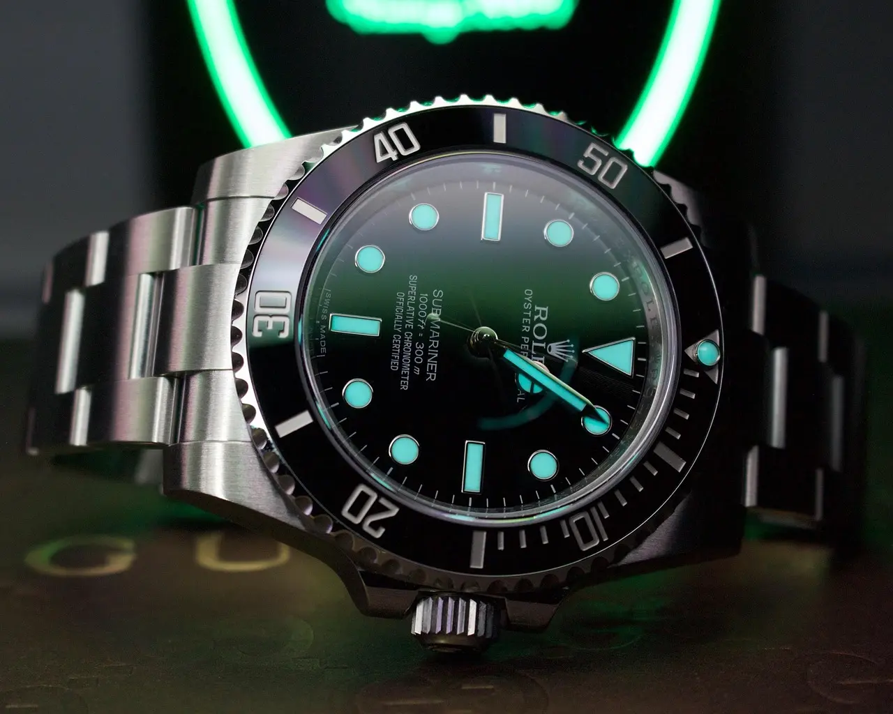 Rolex diver's watch with glowing blue Chromalight lume, black bezel, and stainless steel bracelet.