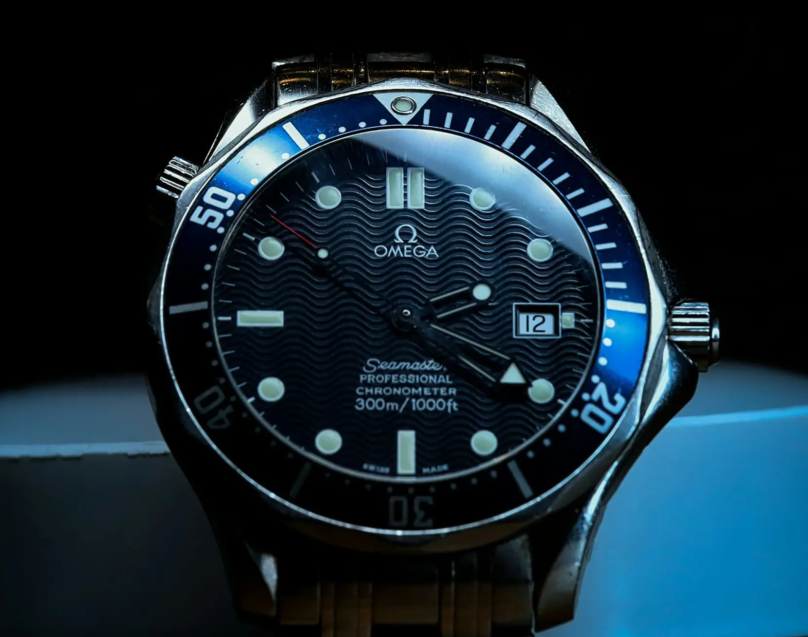 Omega Seamaster dive watch with blue bezel, wavy black dial, and luminous markers; date window at 3 o'clock