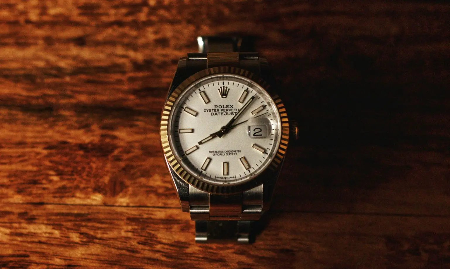 Close-up of a Rolex Oyster Perpetual Datejust wristwatch with a silver dial and fluted gold bezel resting on a wooden surface.