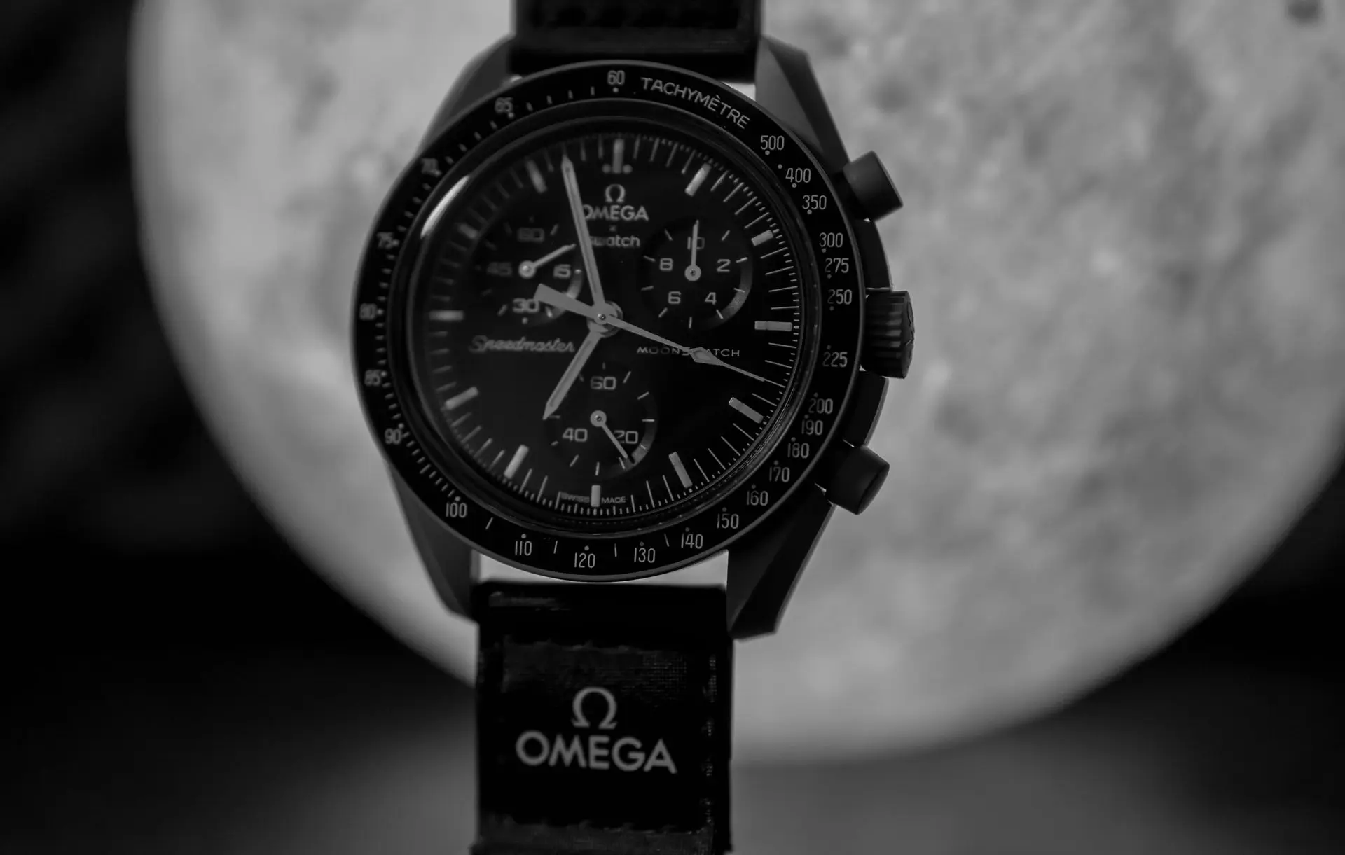 Watch Starter Collection: Omega Speedmaster Chronograph Close-up of a black Omega Speedmaster chronograph watch with a tachymeter bezel and a dark strap, displayed against a blurred background.