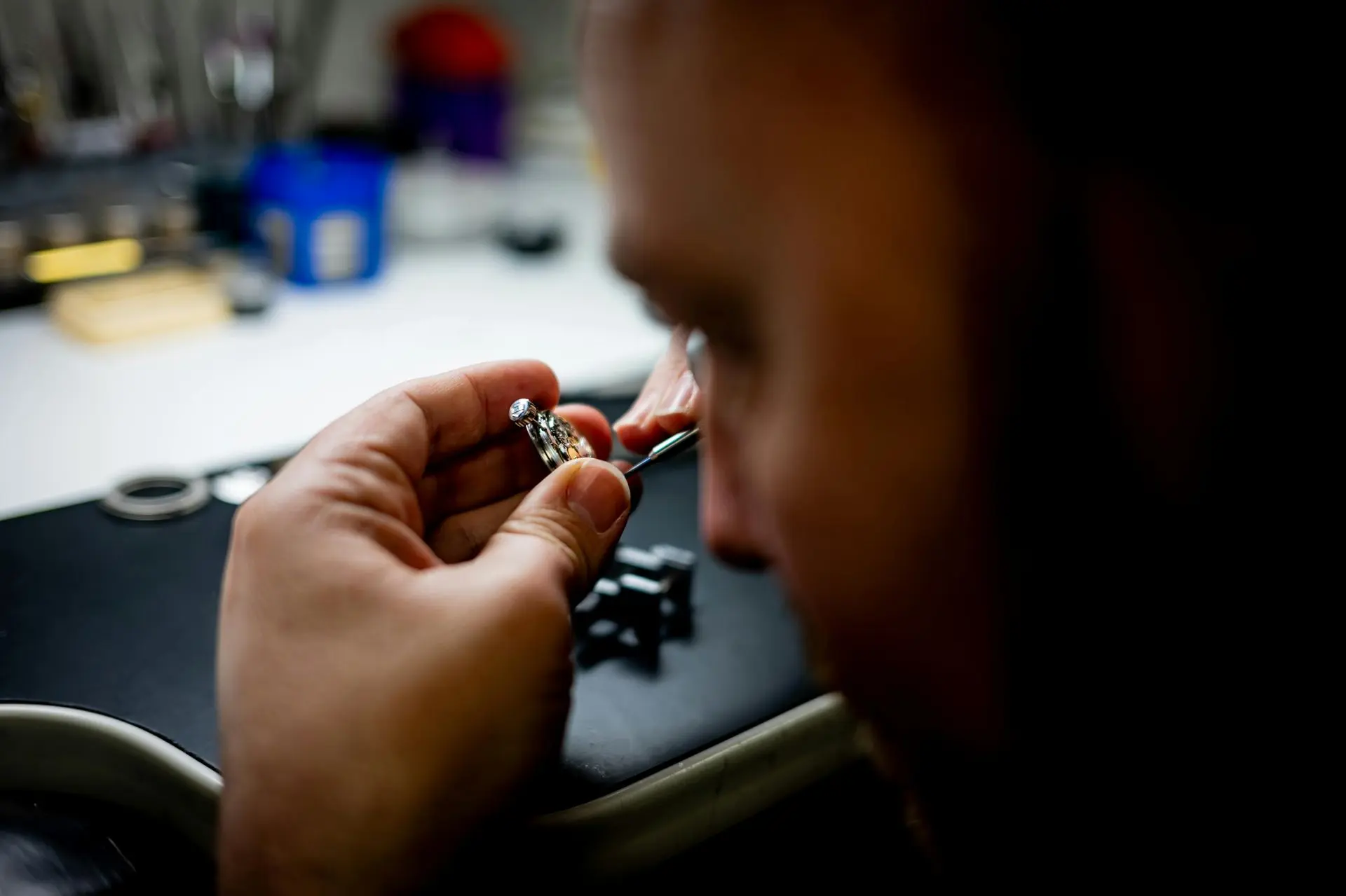 Close-up of a watchmaker assembling a small automatic watch movement at a workbench.