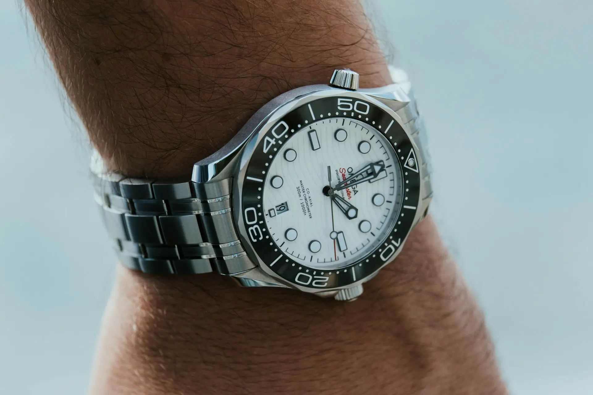  A close-up of a man's wrist wearing a stainless steel Omega dive watch with a white dial and black bezel.