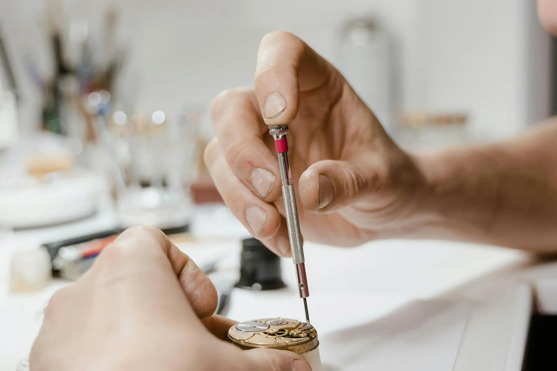 Close-up on watchmaker's hands performing a fine adjustment on a mechanical watch movement with a small screwdriver. Fine Adjustment of Watch Gears