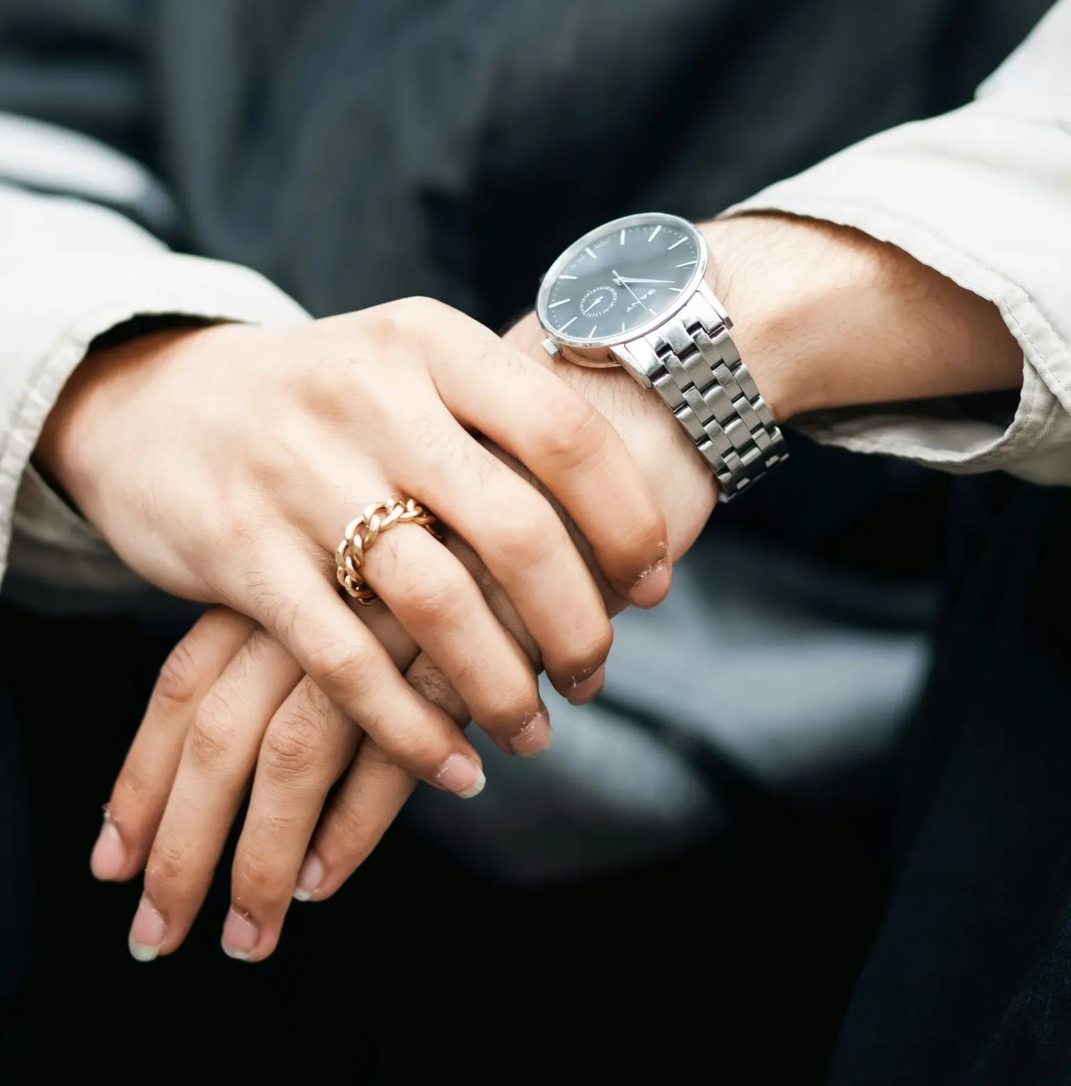 Close-up of a person wearing a silver metal bracelet watch and a gold ring, illustrating how metal watch materials pair with business casual and smart casual outfits.