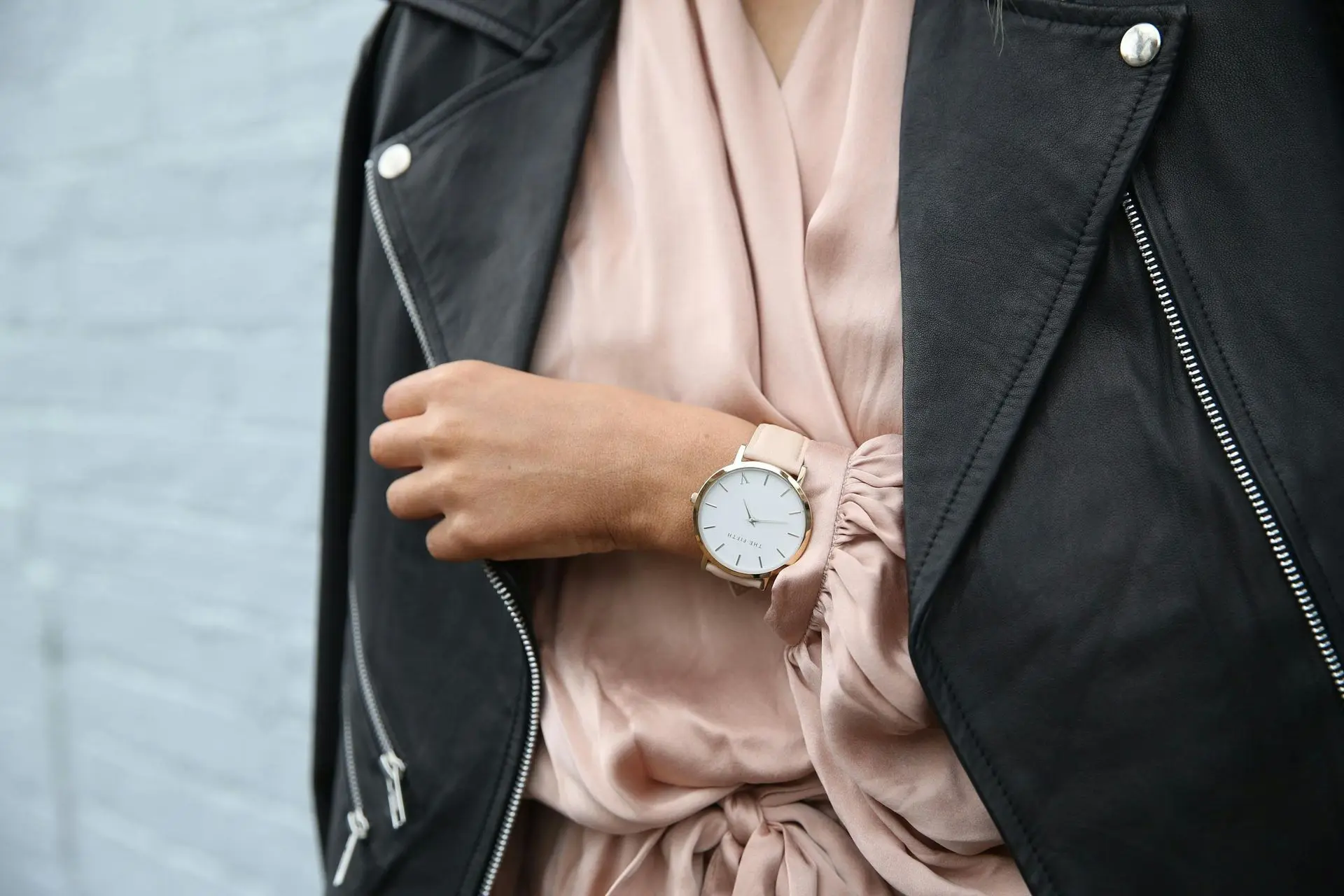 Person wearing a light-colored watch with a pastel strap paired with a soft pink blouse and black jacket, illustrating how seasonal watch dress codes use lighter tones for spring and summer outfits.