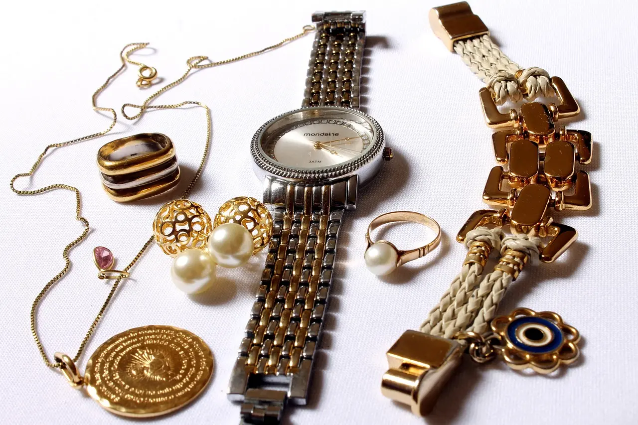 Flat lay of gold and silver accessories including a two-tone metal watch, rings, necklaces, and bracelets, demonstrating accessory coordination rules for matching metals with watches and other jewelry.