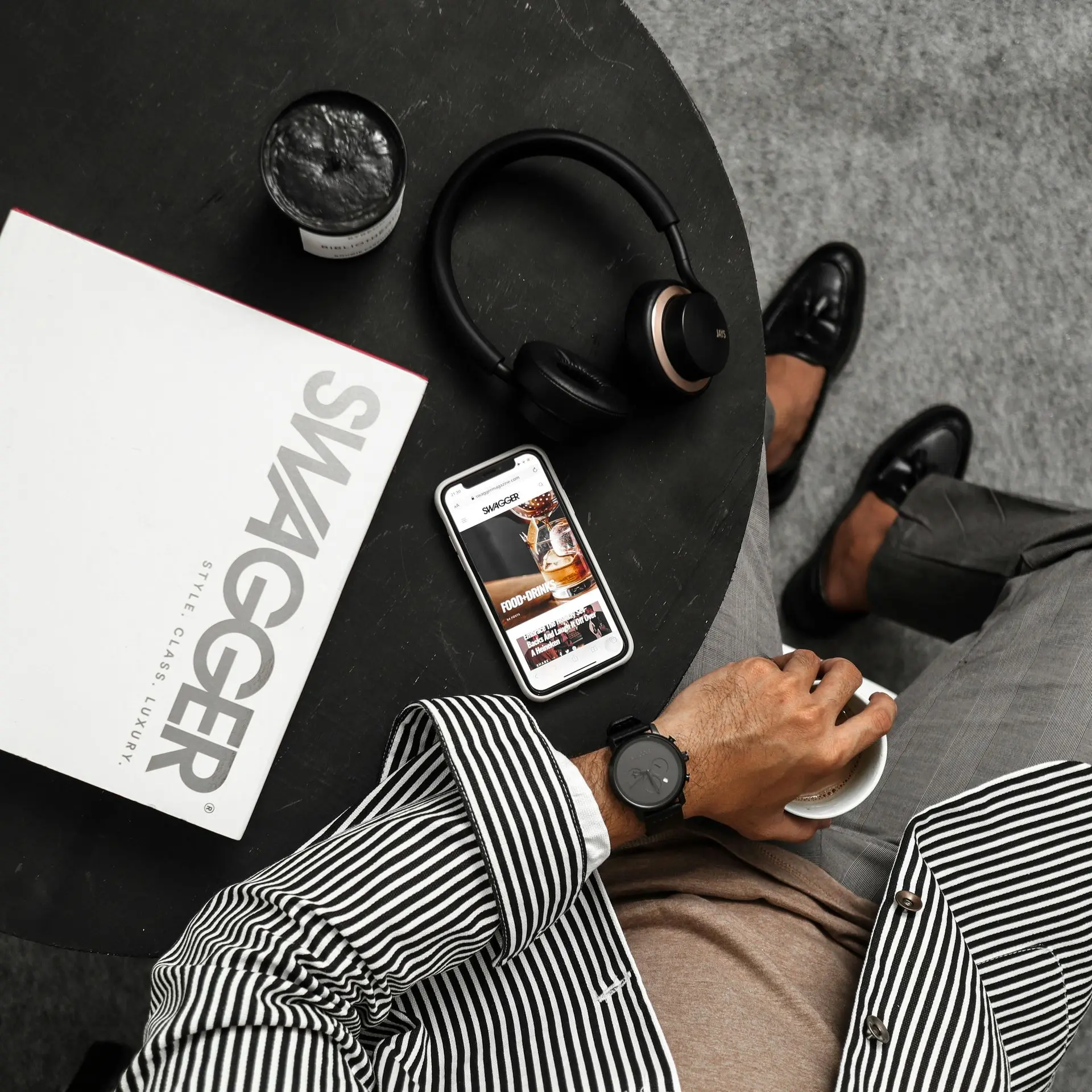 Man wearing a modern black minimalist watch paired with a striped blazer, loafers, and tech accessories, showcasing how different watch styles match various personal fashion aesthetics.