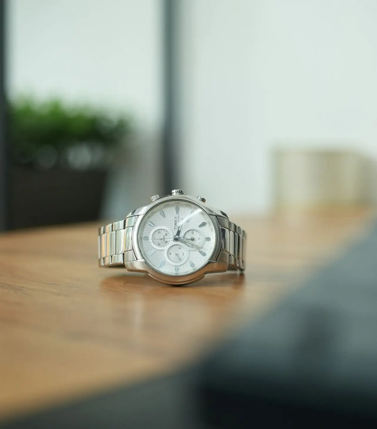 Stainless steel wristwatch on a wooden table in soft natural light for watch photography lighting techniques.