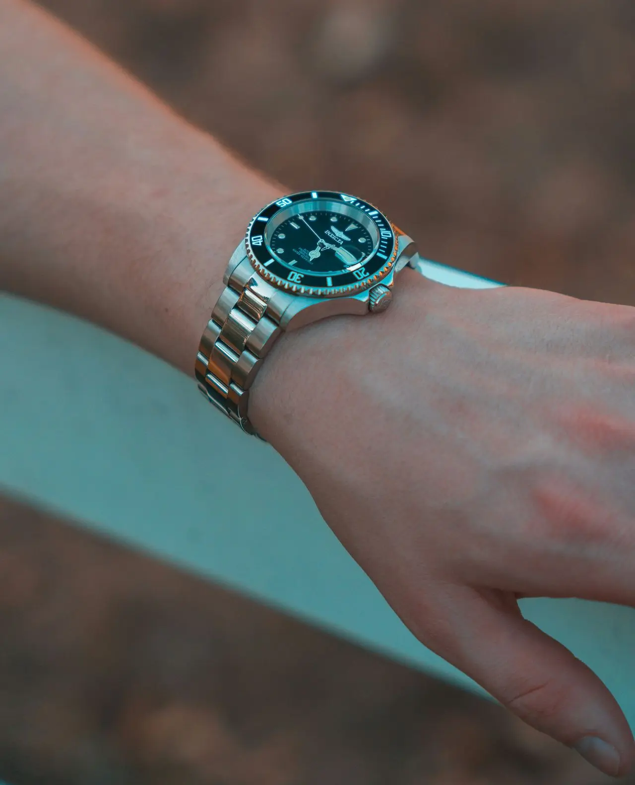 Close-up of a person wearing a stainless steel automatic wristwatch with a black dial outdoors.