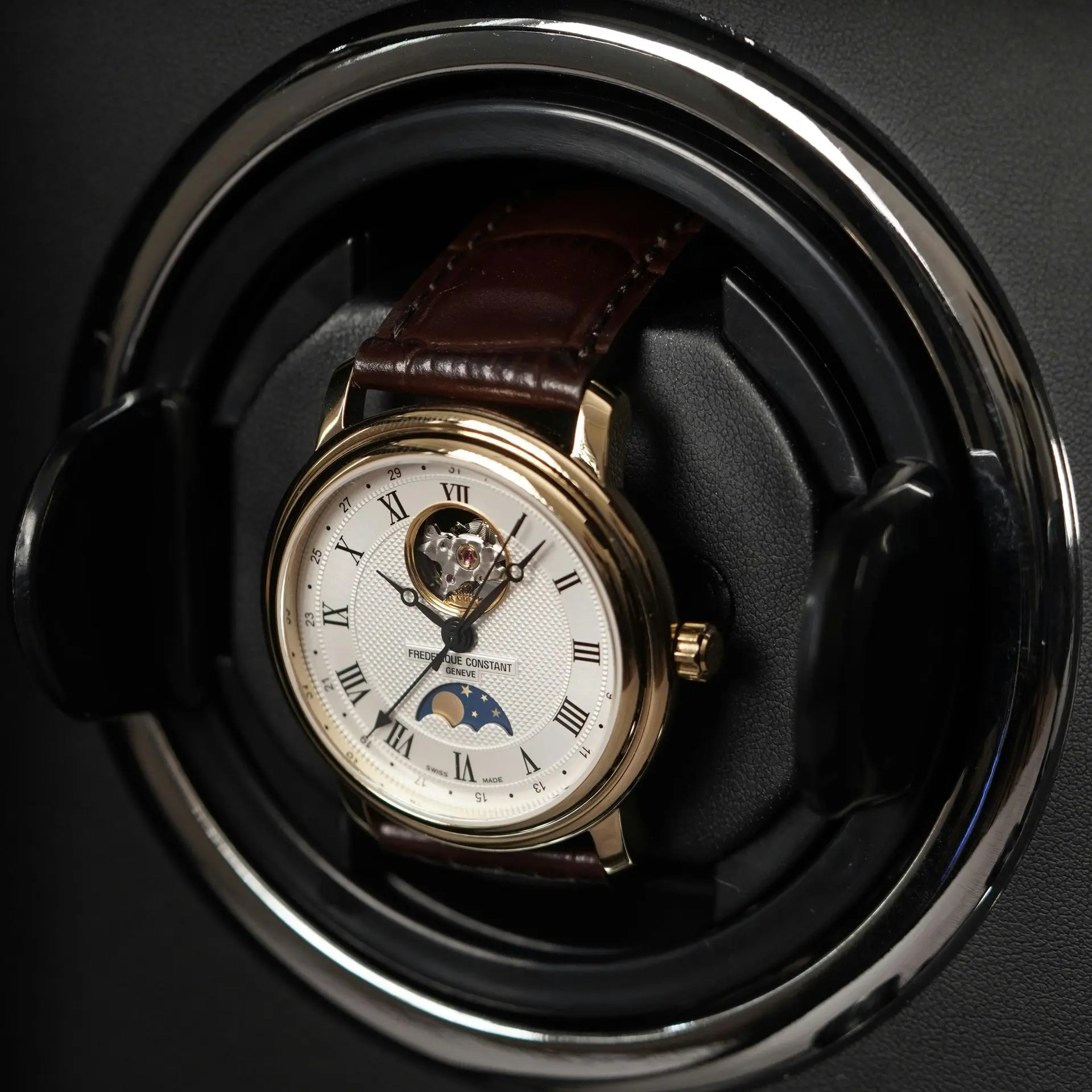 Automatic wristwatch with moonphase displayed inside a watch winder with a leather strap.