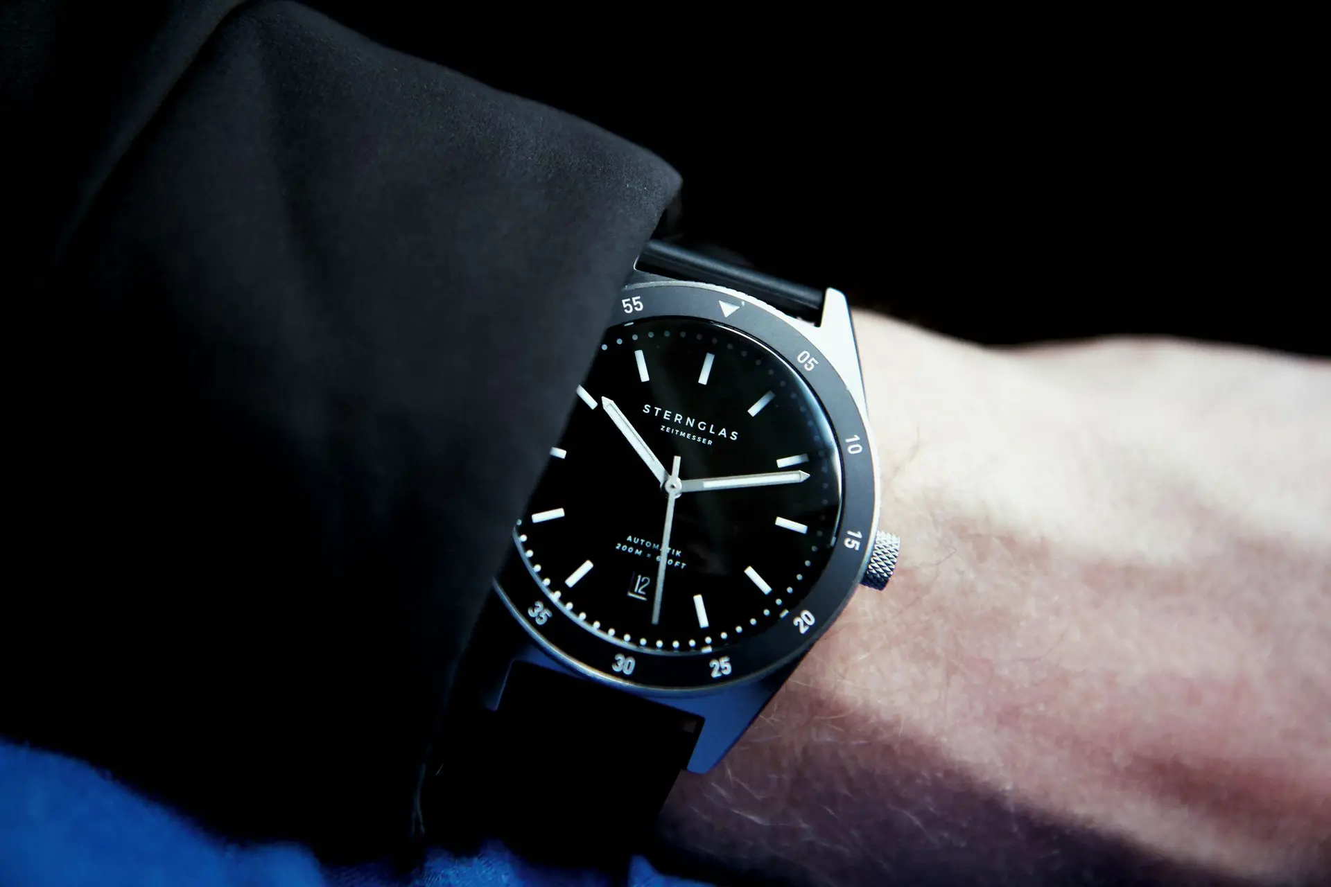 Close-up of a person wearing a black automatic wristwatch with a suit, highlighting everyday use and style.