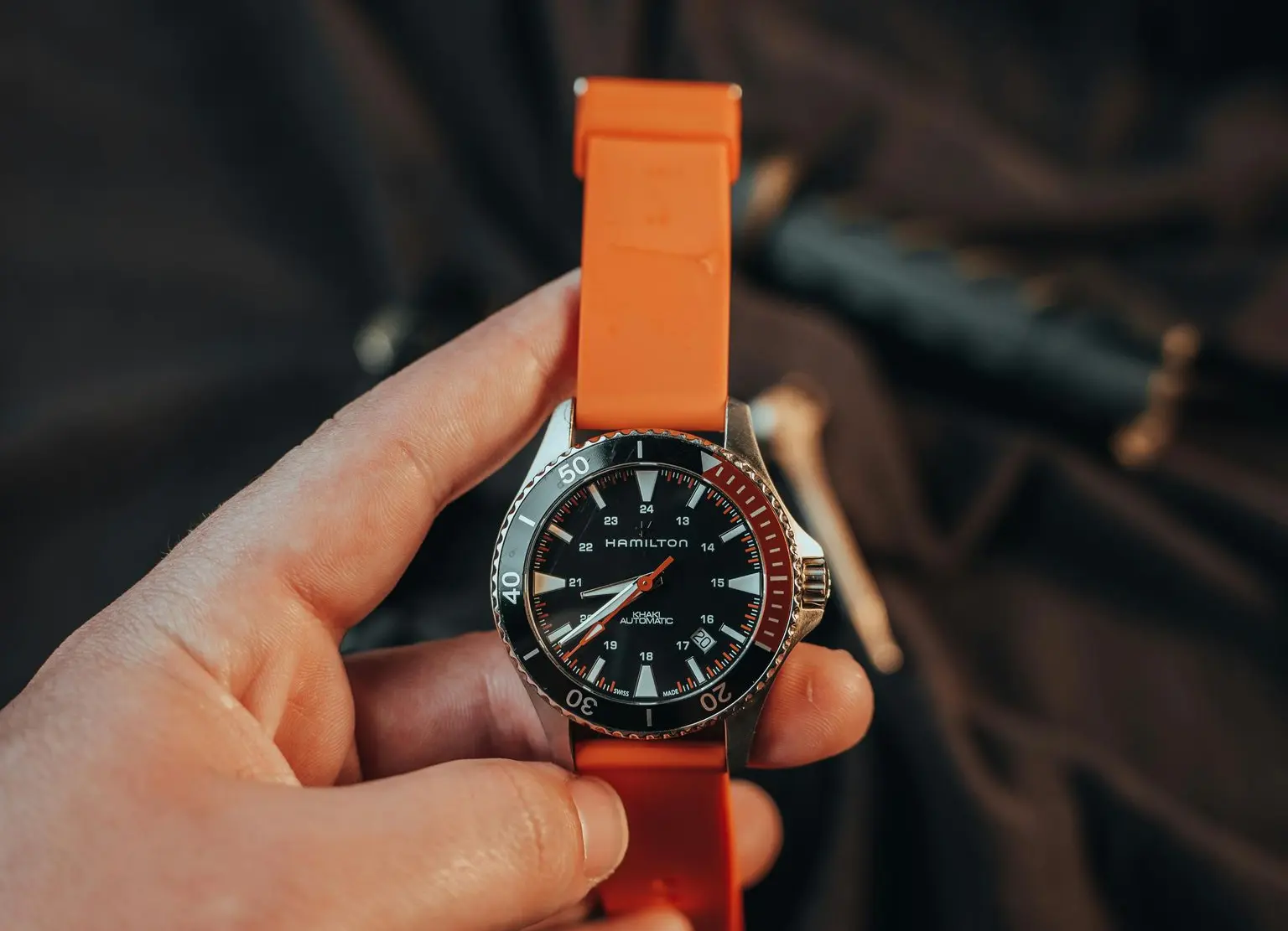 Hamilton field watch with black dial and orange rubber strap held in hand