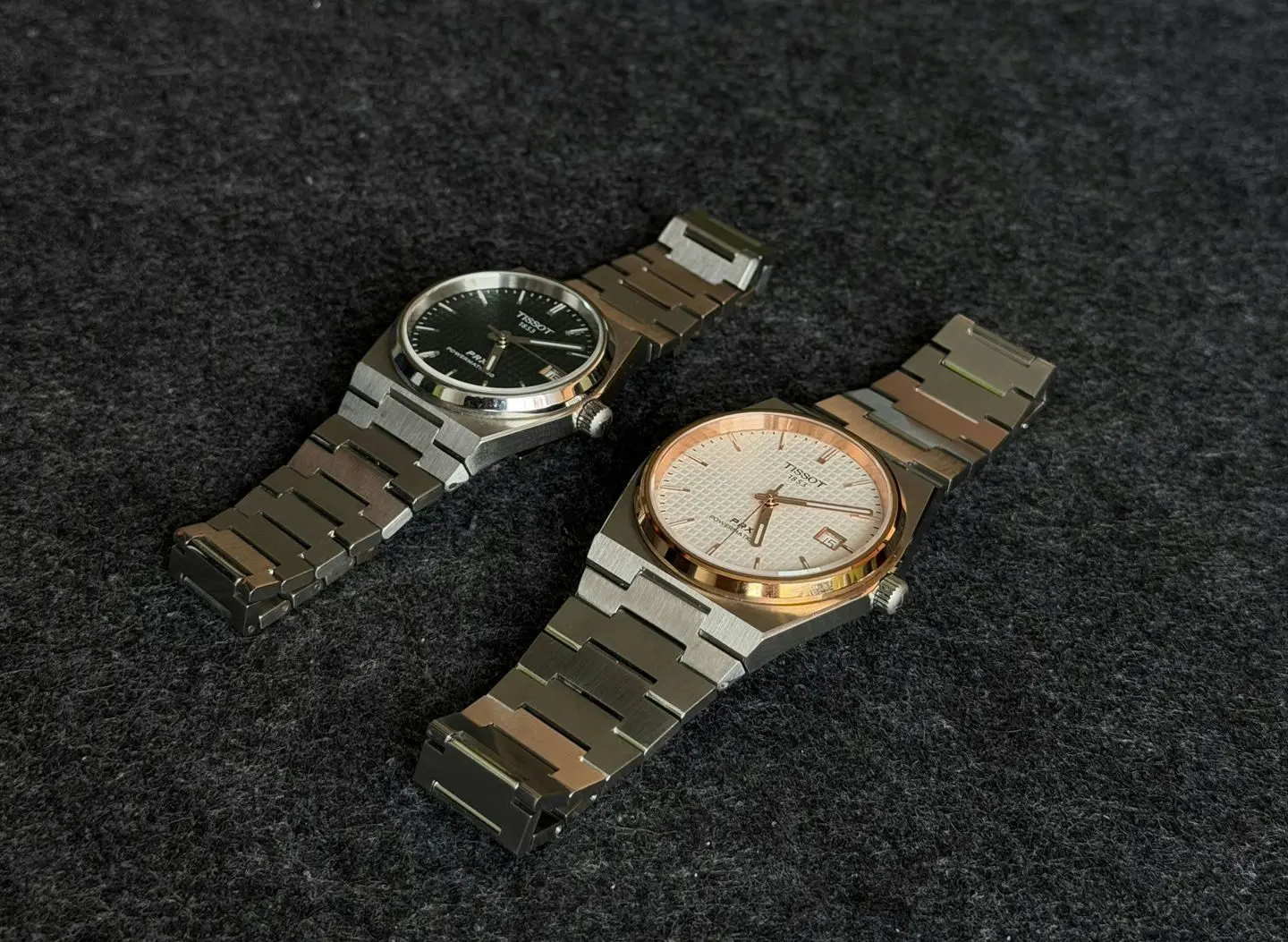 Two Tissot automatic watches with stainless steel bracelets displayed on fabric background