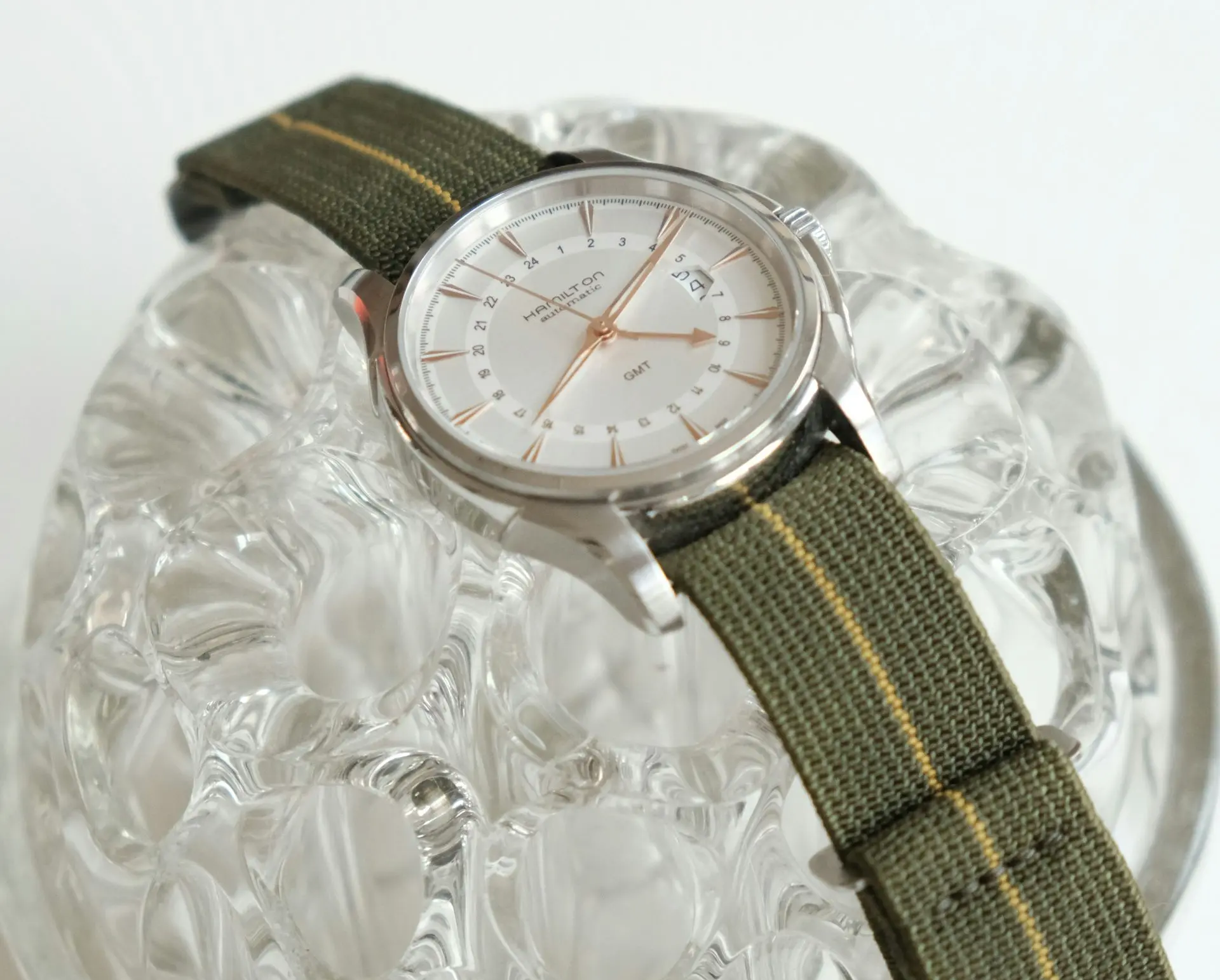 Hamilton GMT watch with white dial, rose gold hands, and green fabric strap showing dual time zone functionality