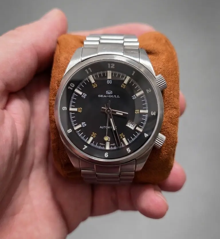 Tianjin Seagull automatic wristwatch with black dial, date display, and stainless steel bracelet held in hand.