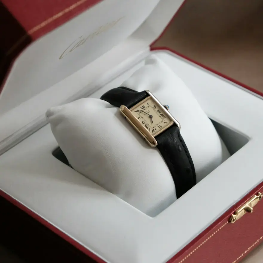 Cartier Tank watch featuring a rectangular gold-tone case, cream dial, Roman numerals, and black leather strap